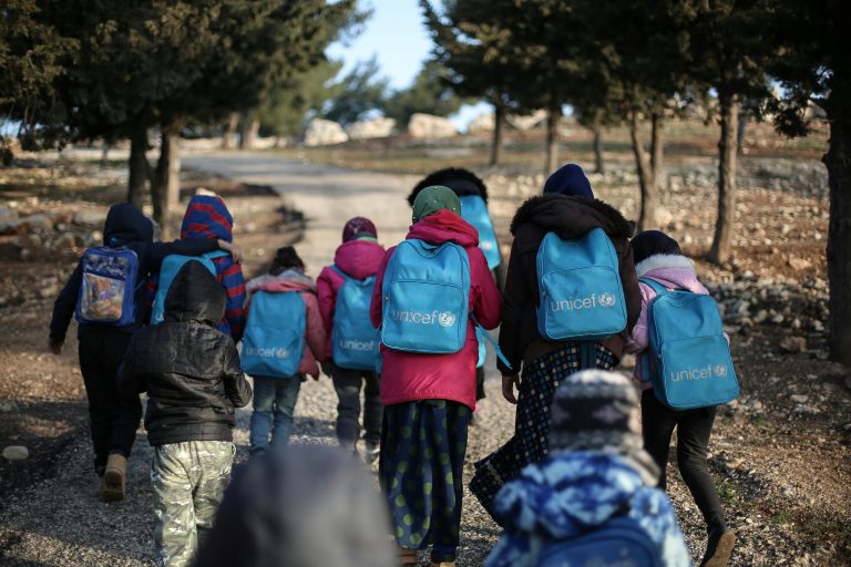 A group of children with UNICEF backpacks walking on a dirt road in rural Syria.